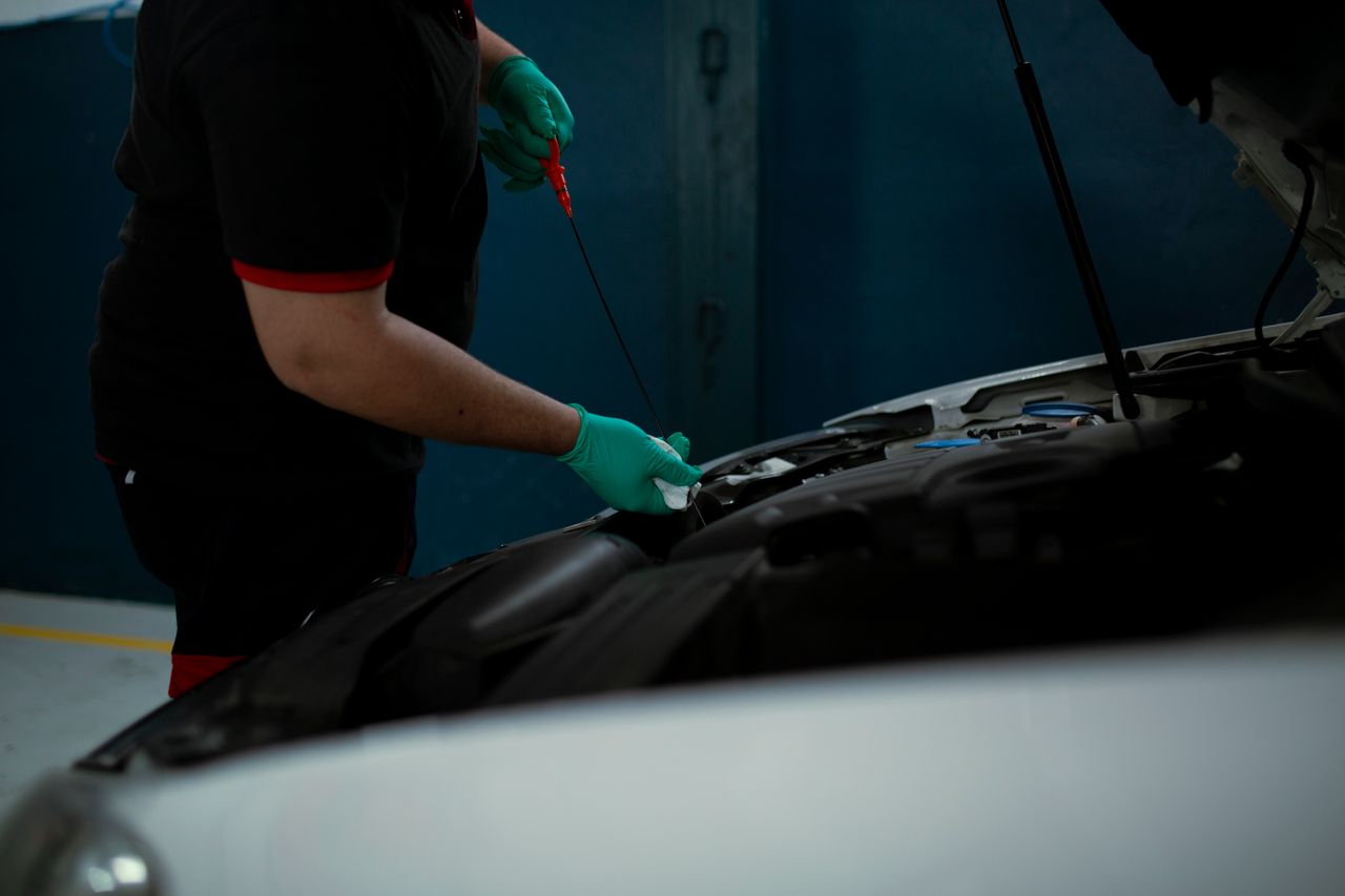Mechanic in gloves checking engine oil level in a vehicle at an indoor workshop.